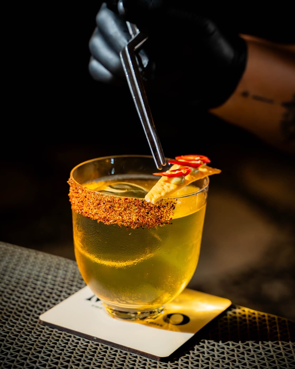 Golden cocktail with a chilli-salt rim being stirred
