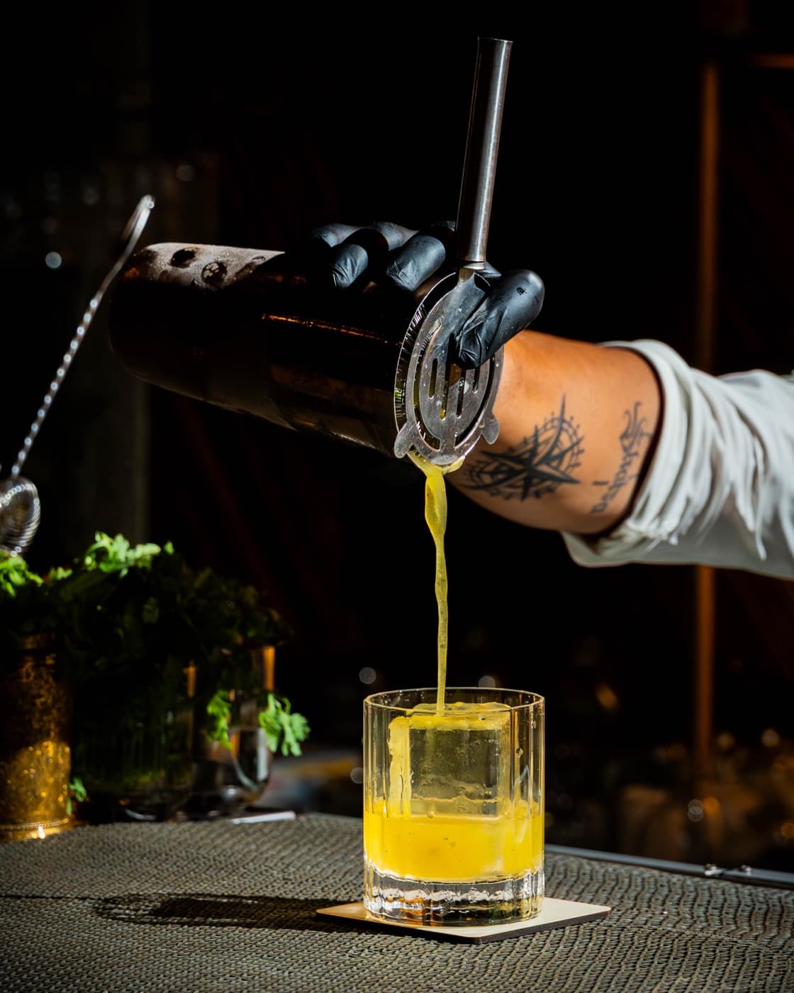Black-gloved bartender pouring a golden cocktail