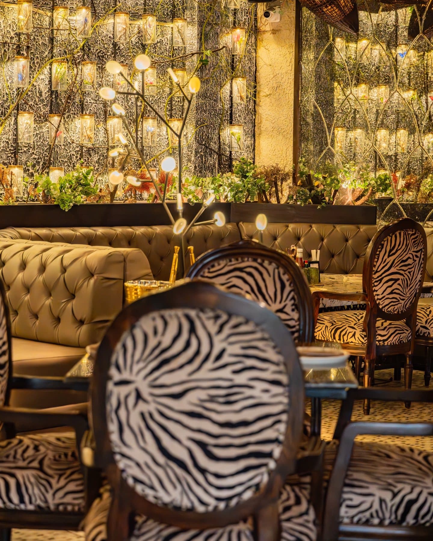 Zebra-print chairs and tufted banquettes before a wall of illuminated apothecary bottles